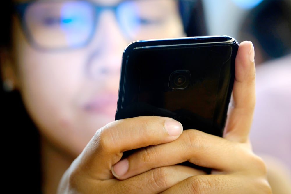 A woman looking closeup at her phone and likely experiencing digital eye strain symptoms, who may someday need glasses for digital eye strain