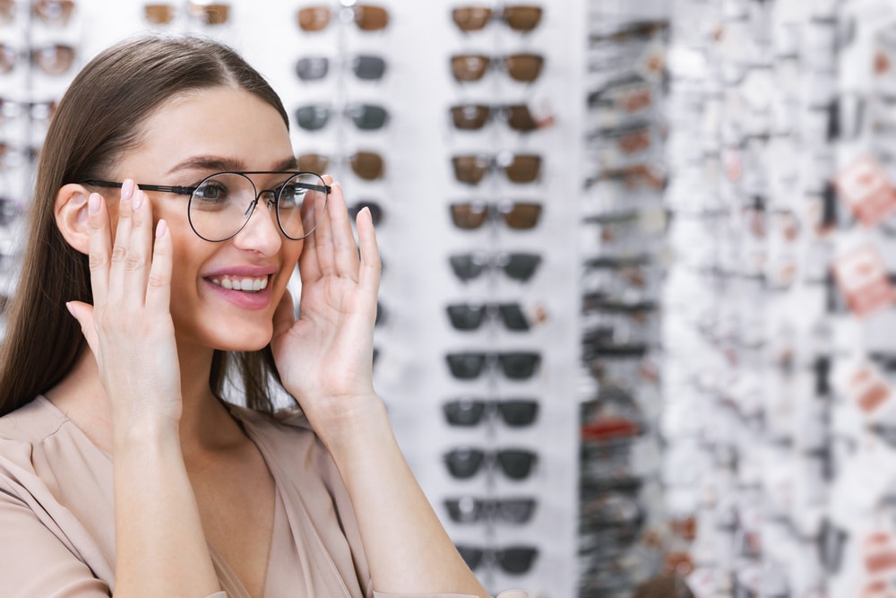 A woman tying on eyeglass frames and trying to choose the best glasses for face shape