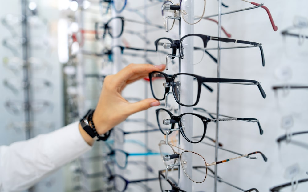 Optometrist choosing a pair of Lafont glasses or similar from a wall of frames.