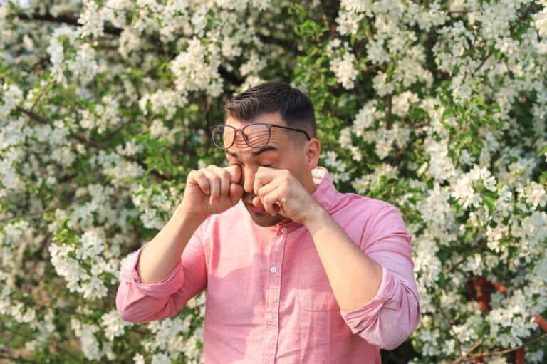 Man rubbing his eyes in front of flowers as allergy season in Nashville affects his eyes